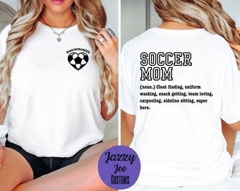 May include: White t-shirt with the text "#soccermomlife" and a soccer ball inside a heart on the front. The back of the shirt has the text "SOCCER MOM (noun.) Cleat finding, uniform washing, snack getting, team loving, carpooling, sideline sitting, super hero."