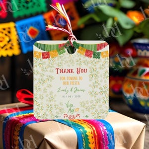 May include: A square gift tag with a festive Mexican fiesta theme. The tag features the text "Thank You for coming to our Fiesta" with names and a date. It is decorated with colorful papel picado banners and floral accents. The tag is tied with a red and white string.
