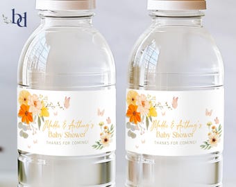 May include: Two clear plastic water bottles with labels featuring a floral design in shades of orange, yellow, and pink. The labels also include the text "Maddie & Anthony's Baby Shower" and "Thanks for coming!"