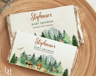 May include: Two chocolate bar wrappers with a woodland theme. The wrappers are white with brown text that says "Stephanie's Baby Shower Thanks for coming!" and feature a watercolor illustration of a forest with mountains, trees, and animals.