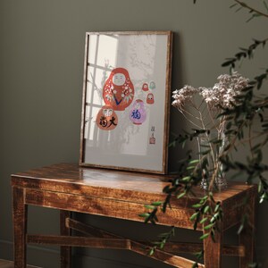 May include: A framed print featuring a collection of Daruma dolls in various sizes and colors. The largest doll is red with white floral accents, while others are purple, green, and orange. Japanese characters are visible on some of the dolls.