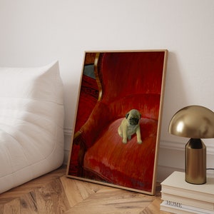 Puede incluir: Impresi&oacute;n enmarcada de un cachorro de pug sentado en un sill&oacute;n de terciopelo rojo. El marco de madera se apoya en una pared blanca. Una l&aacute;mpara dorada y libros se ven en el fondo, creando un ambiente acogedor.