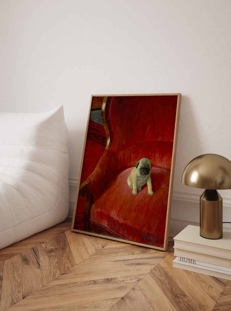 Puede incluir: Impresi&oacute;n enmarcada de un cachorro de pug sentado en un sill&oacute;n de terciopelo rojo. El marco de madera se apoya en una pared blanca. Una l&aacute;mpara dorada y libros se ven en el fondo, creando un ambiente acogedor.