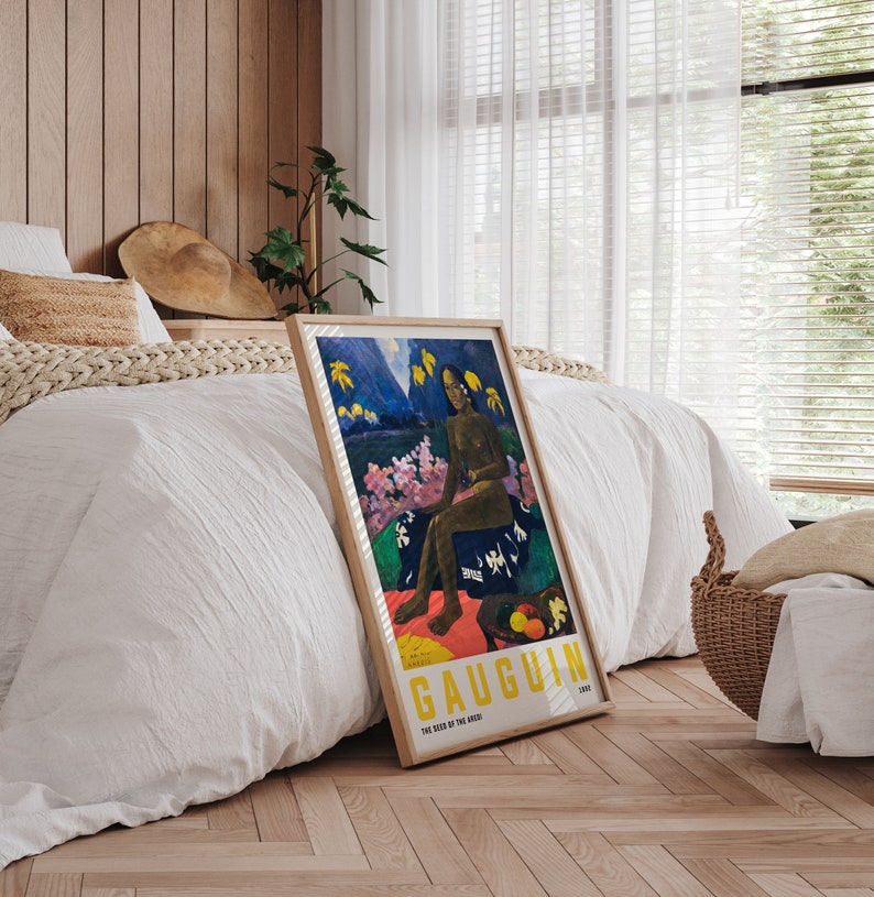 May include: A framed art print of Gauguin's "The Seed of the Areoi" featuring a seated figure in a tropical landscape. The artwork has a wooden frame and is propped against a bed with white bedding. The print includes yellow text.