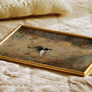 K&ouml;nnte beinhalten: Ein gerahmtes Kunstwerk mit einer schwarz-wei&szlig;en Katze in einem Feld mit hohem Gras. Das Gem&auml;lde hat einen goldenen Rahmen und liegt auf einer cremefarbenen, gemusterten Oberfl&auml;che. Das Kunstwerk zeigt eine Katze in einer nat&uuml;rlichen Umgebung.