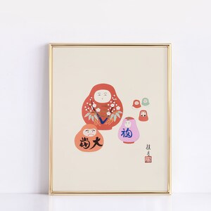 May include: A framed print featuring several Daruma dolls in various sizes and colors. The largest doll is red with white floral accents. Other dolls are orange, pink, and green. Japanese characters are visible on the dolls and in the lower right corner.