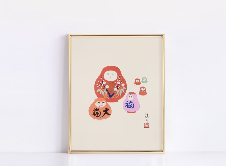 May include: A framed print featuring several Daruma dolls in various sizes and colors. The largest doll is red with white floral accents. Other dolls are orange, pink, and green. Japanese characters are visible on the dolls and in the lower right corner.