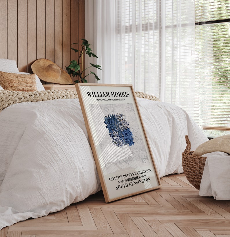 May include: A framed poster featuring the text "WILLIAM MORRIS THE VICTORIA AND ALBERT MUSEUM" and "COTTON PRINTS EXHIBITION NEAREST SOUTH KENSINGTON STATION". The poster has a light beige frame and displays a blue floral design.
