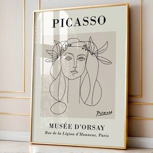 Puede incluir: Una impresi&oacute;n art&iacute;stica enmarcada con un dibujo lineal de Picasso de un rostro femenino con una corona floral. La impresi&oacute;n tiene un fondo beige con la palabra "PICASSO" en la parte superior y "MUS&Eacute;E D'ORSAY" en la parte inferior. El marco es dorado.