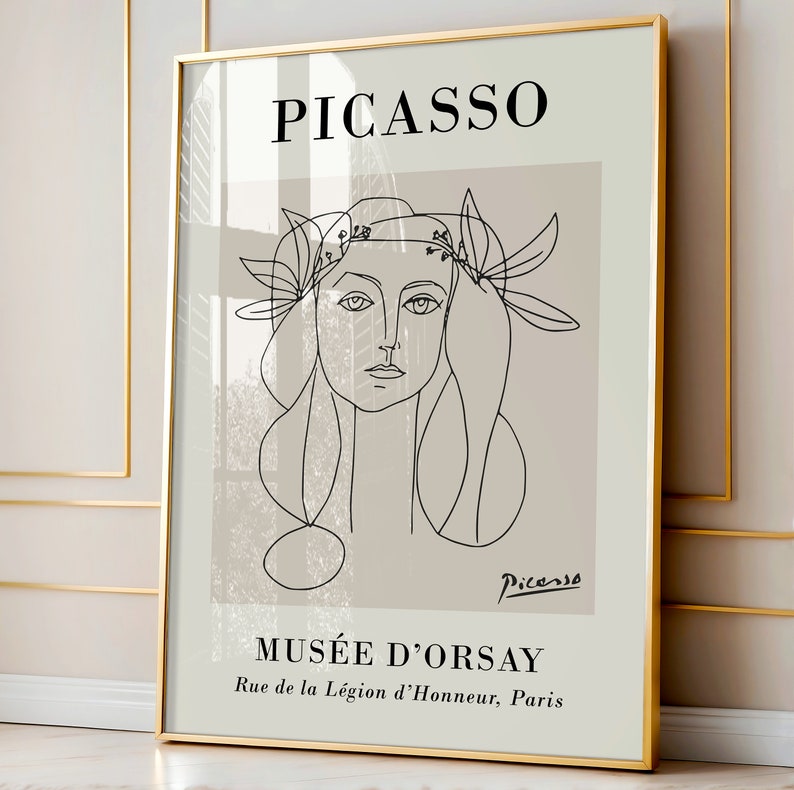 Puede incluir: Una impresi&oacute;n art&iacute;stica enmarcada con un dibujo lineal de Picasso de un rostro femenino con una corona floral. La impresi&oacute;n tiene un fondo beige con la palabra "PICASSO" en la parte superior y "MUS&Eacute;E D'ORSAY" en la parte inferior. El marco es dorado.