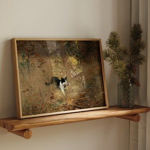 K&ouml;nnte beinhalten: Gerahmter Kunstdruck mit einer schwarz-wei&szlig;en Katze in einer Waldszene, die Beute tr&auml;gt. Das Kunstwerk befindet sich in einem Holzrahmen und steht auf einem Holzregal. Rechts befindet sich eine Glasvase mit Kiefernzweigen und Zapfen.