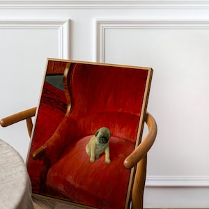 Puede incluir: Una impresi&oacute;n enmarcada que presenta un cachorro pug sentado en un sill&oacute;n rojo. La obra de arte tiene una paleta de colores c&aacute;lidos, con el pelaje canela del perro contrastando con el rojo intenso de la silla. El marco es de color madera clara.