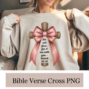 Op de afbeelding: Beige sweatshirt met een houten kruisontwerp, een roze lint en de Bijbeltekst "Wees niet bevreesd, want Ik ben met u - Jesaja 41:10". Het ontwerp is gecentreerd. De woorden "Bible Verse Cross PNG" staan onderaan.