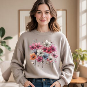 Puede incluir: Su&eacute;ter beige con un dise&ntilde;o floral con flores rosas, blancas, azules y naranjas. Las flores est&aacute;n agrupadas y tienen detalles delicados. El su&eacute;ter tiene cuello redondo y mangas largas.