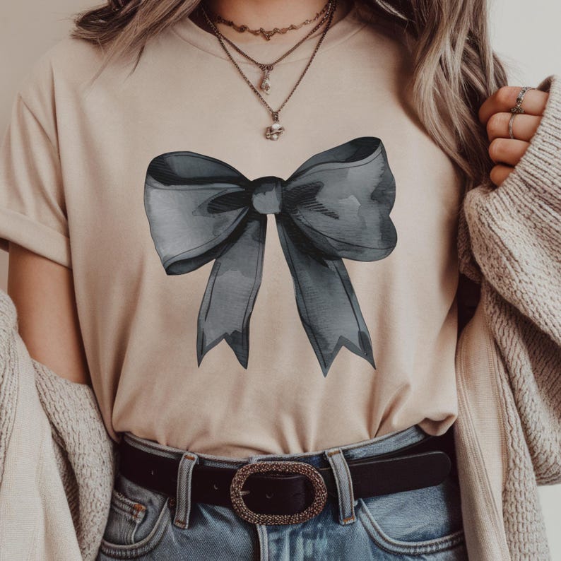 May include: A beige t-shirt with a large, dark gray watercolor bow design. The bow is tied in a knot and the ends are flowing down.
