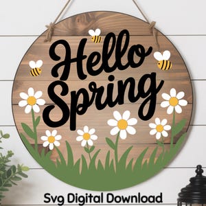 May include: Round wooden sign with the words "Hello Spring" in black script. The sign features white daisies with yellow centers, green grass, and yellow and black bees. The text "Svg Digital Download" is at the bottom.