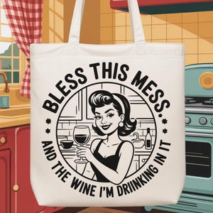 May include: Off-white tote bag with the text "BLESS THIS MESS...AND THE WINE I'M DRINKING IN IT." The graphic features a retro-style woman holding a wine glass. The bag has two white handles.