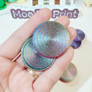 May include: A set of three iridescent, multi-colored, round, decorative,  spinning tops. The tops have a concentric circle pattern with a metallic sheen.