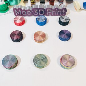 May include: Nine different colored round buttons with a swirl design. The buttons are arranged in a grid pattern on a white surface. The buttons are made of plastic and have a smooth finish.