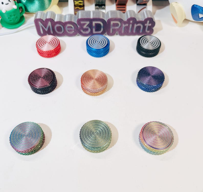 May include: Nine different colored round buttons with a swirl design. The buttons are arranged in a grid pattern on a white surface. The buttons are made of plastic and have a smooth finish.
