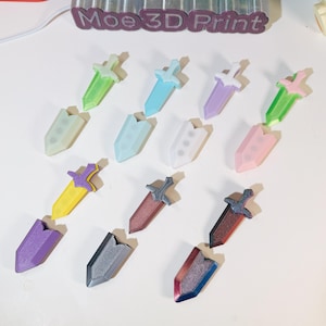 Könnte beinhalten: Eine Sammlung von 12 kleinen, 3D-gedruckten Schwertern in verschiedenen Farben, darunter Grün, Blau, Lila, Weiß, Rosa, Gelb, Rot, Grau und Blau. Die Schwerter sind in zwei Reihen auf einer weißen Oberfläche angeordnet. Der Text "Moe 3D Print" ist im Hintergrund sichtbar.