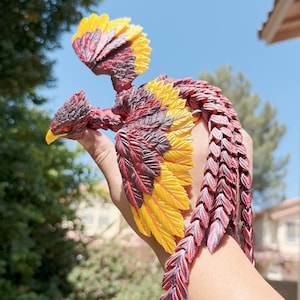 May include: A red and yellow phoenix figurine with detailed wings and a long tail. The figurine is made of a textured material and has a realistic appearance.