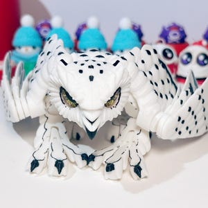 May include: A white and black plastic owl toy with articulated wings and legs. The owl has yellow eyes and a black beak.