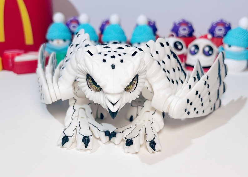 May include: A white and black plastic owl toy with articulated wings and legs. The owl has yellow eyes and a black beak.
