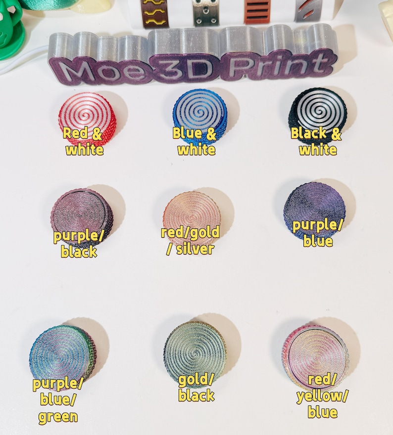 May include: Nine different color combinations of 3D printed round buttons with a spiral design. The colors include red and white, blue and white, black and white, purple and black, red and gold, purple and blue, purple, blue and green, gold and black, and red, yellow and blue.