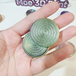 May include: Two round, green and gold, layered, decorative coasters with a spiral pattern.