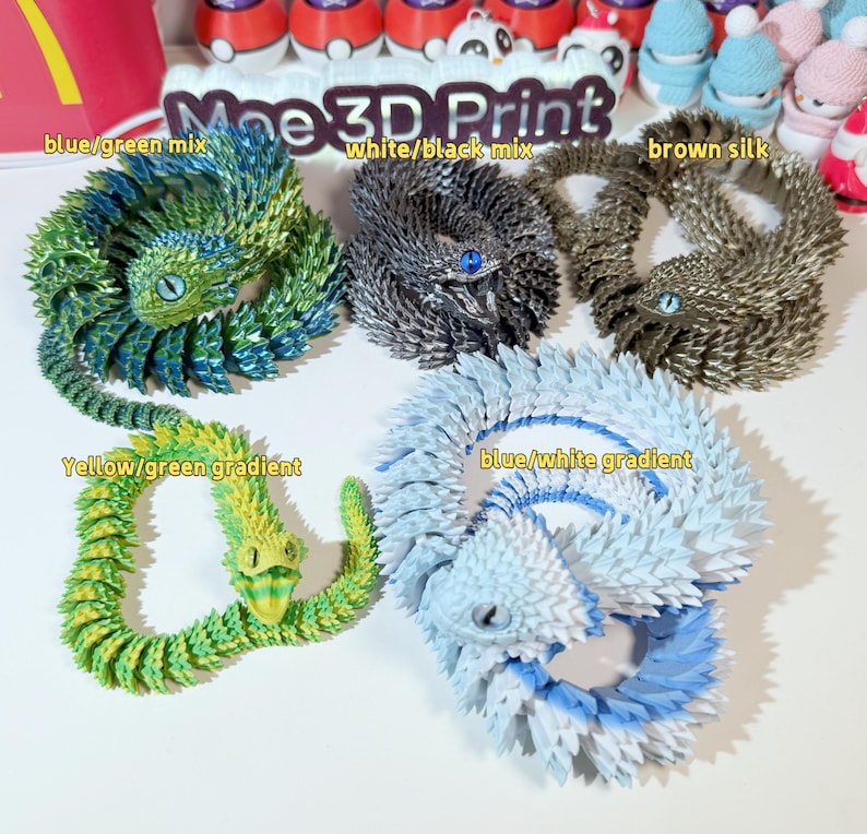 May include: Five 3D printed models of a lizard-like creature in different color combinations. The colors include blue and green, white and black, brown, yellow and green, and blue and white.