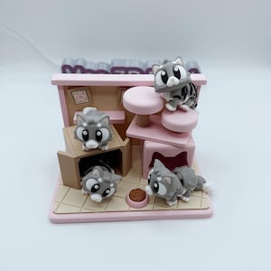 Puede incluir: Un juego de casa para gatos en miniatura con cuatro figuras de gatitos grises y blancos. El juego presenta una base rosa, una pequeña caja marrón y un árbol para gatos rosa con dos plataformas rosas. También se incluye un pequeño cuenco de comida marrón.