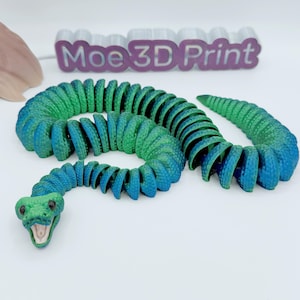 Op de afbeelding: Een 3D-geprint, beweeglijk slangen speelgoed in blauw- en groentinten. De slangenkop is groen met een open mond, en het lichaam gaat over van groen naar blauw. De tekst "Moe 3D Print" is zichtbaar op de achtergrond.