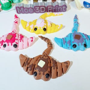 May include: Four colorful 3D printed stingray figurines with chocolate bar accents. The stingrays are pink, yellow, blue, and brown.