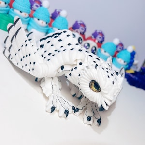 May include: A white and black owl figurine with a yellow eye. The owl is perched on a white surface and has a detailed design.