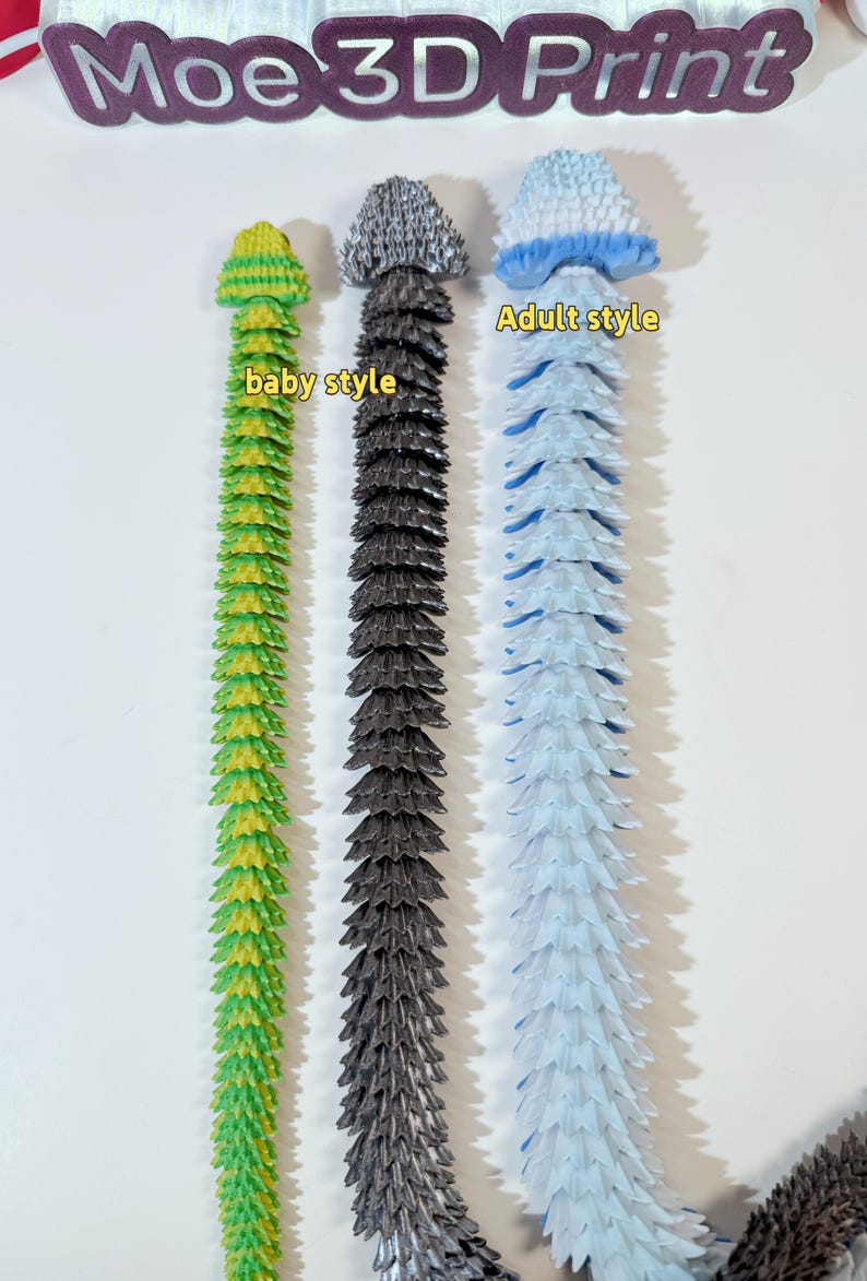 May include: Three 3D printed flexible toys in different colors and styles. The toy on the left is green and yellow and labeled "baby style". The middle toy is gray and the toy on the right is blue and white and labeled "Adult style".