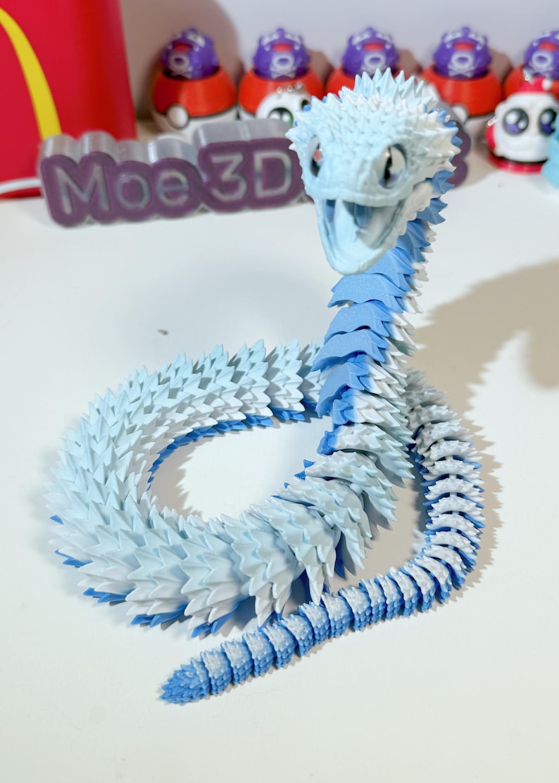 May include: A 3D printed blue and white snake figurine with a spiky texture. The snake is curled up in a circle with its head raised. The figurine is made of plastic and is about 10 inches long.