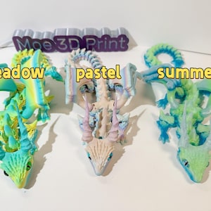 May include: Three 3D printed dragon figurines in different color schemes. The first dragon is green and yellow with the word "meadow" in front of it. The second dragon is white and blue with the word "pastel" in front of it. The third dragon is green and blue with the word "summer" in front of it.