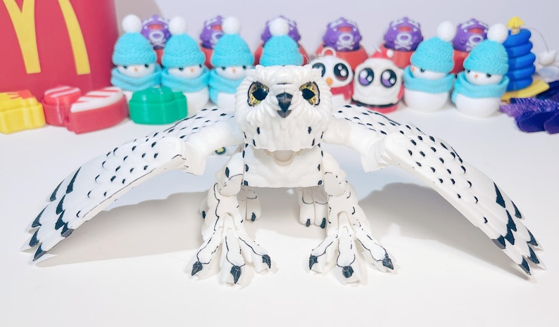 May include: A white and black articulated owl toy with large, black eyes. The owl has its wings spread out and is posed in a standing position.