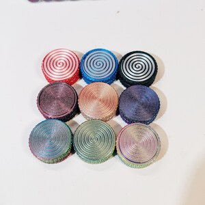 May include: Nine round, colorful, decorative, spiral patterned, metal, trinkets. The trinkets are arranged in a square shape.
