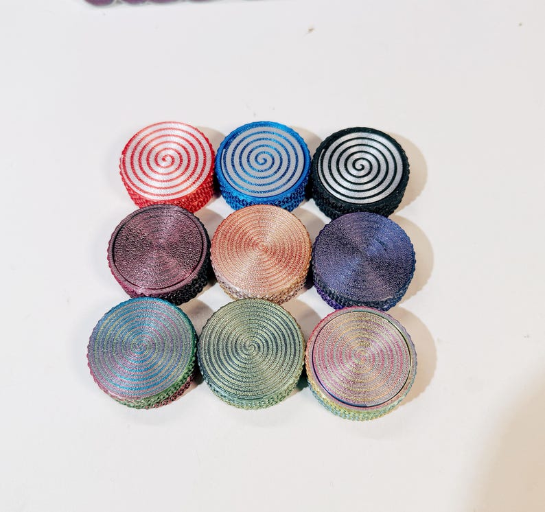 May include: Nine round, colorful, decorative, spiral patterned, metal, trinkets. The trinkets are arranged in a square shape.