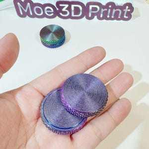 May include: Two iridescent purple fidget spinners with a textured surface. The spinners are in a hand.