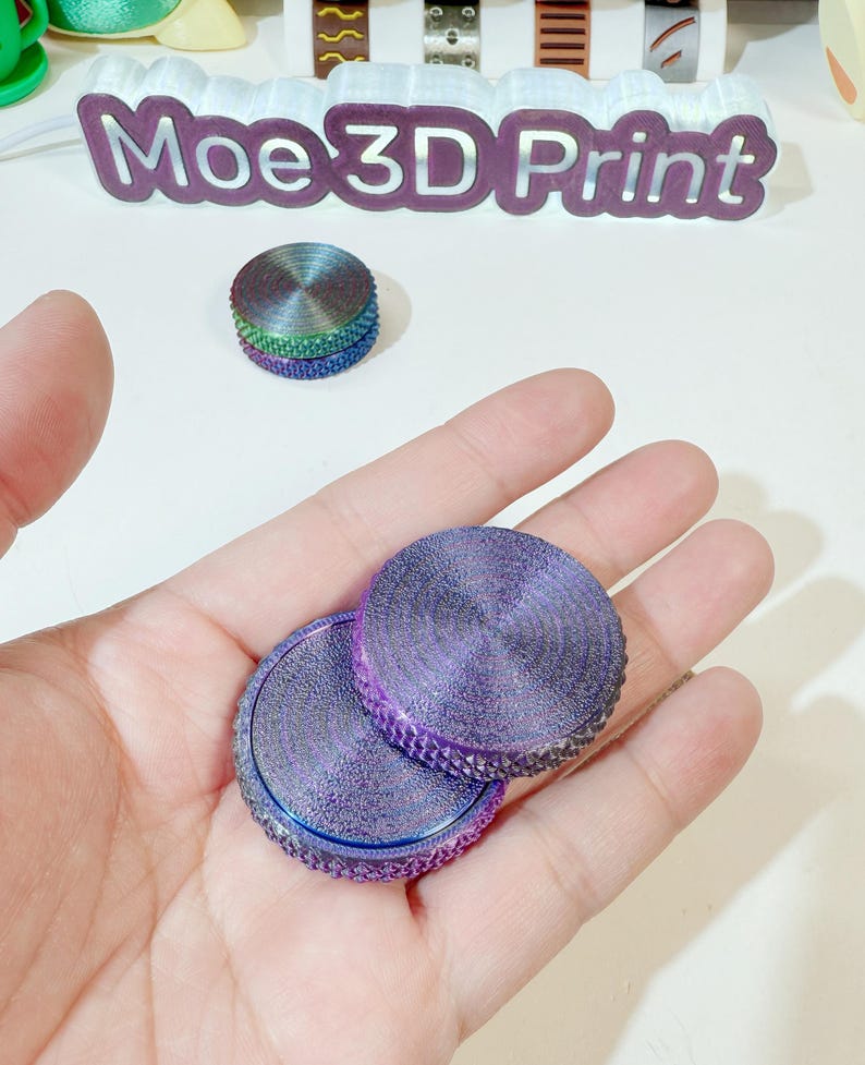 May include: Two iridescent purple fidget spinners with a textured surface. The spinners are in a hand.
