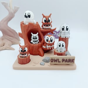 May include: A whimsical Owl Park diorama featuring seven owl figurines in various colours. The owls are perched on a brown tree structure and stumps, with a sign that reads "OWL PARK". The base is a light tan colour.