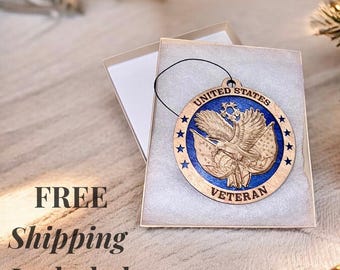 May include: A wooden ornament with a blue background and a bald eagle with American flags. The ornament says "United States Veteran" in a white circle around the eagle.