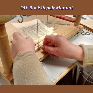 May include: A wooden bookbinding sewing frame with vertical threads and a needle being used to stitch pages of a book. The image includes the text FIX AND BIND YOUR OWN BOOKS, DIY Book Repair Manual, and Digital Download Printable.
