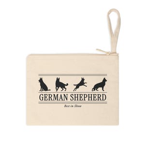 May include: A beige canvas zipper pouch featuring a black graphic of four German Shepherd silhouettes in various poses. The text GERMAN SHEPHERD is printed in a bold serif font, with the words Best in Show written below in a smaller italicized font.