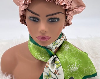 May include: A pink satin sleep cap with a green and white floral patterned silk scarf. The scarf has a green border and a tag that reads "Bare Heritage, Pure Mulberry Silk, Bareheritage.com".