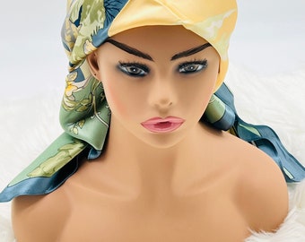 May include: A yellow and green patterned silk headscarf tied in a knot on a mannequin head. The scarf has a floral design with a light blue background.