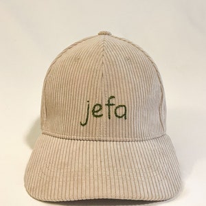 May include: A beige corduroy baseball cap with the word "jefa" embroidered in green thread.